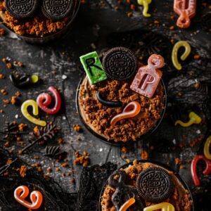 Graveyard Dirt Cups with Oreo cookie tombstones in clear cups topped with gummy worms and Halloween sprinkles