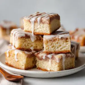 Cinnamon Roll Bliss Bars 2 Freshly baked cinnamon roll bliss bars swirled with cinnamon sugar and drizzled with cream cheese glaze, cut into squares on a wooden board.