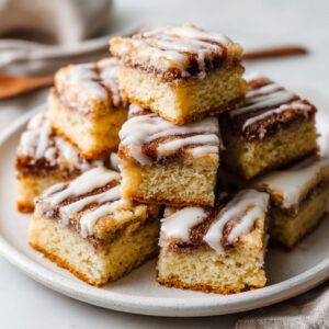 Cinnamon Roll Bliss Bars 3 Freshly baked cinnamon roll bliss bars swirled with cinnamon sugar and drizzled with cream cheese glaze, cut into squares on a wooden board.