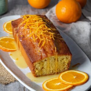 Glazed orange loaf cake topped with citrus glaze on a wooden cutting board
