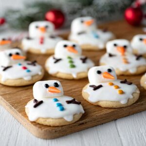 Decorated Melted Snowman Cookies with marshmallow heads, icing, and candy on a sugar cookie base