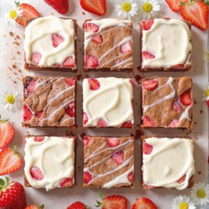 Fudgy strawberry brownies topped with creamy frosting and fresh strawberry slices