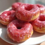 Close-up of air fryer mini donuts with strawberry glaze, stacked on a white plate.