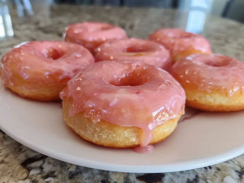Close-up of air fryer mini donuts with strawberry glaze on a white plate.