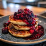 A stack of three fluffy Almond Flour Pancakes topped generously with vibrant berry compote and fresh berries.