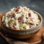 Close-up of a bowl filled with apple cranberry coleslaw, showing the ingredients.