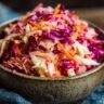 Close-up of a bowl filled with vibrant Apple Cranberry Coleslaw, showcasing shredded cabbage, carrots, and cranberries.