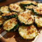 Close-up of golden brown baked parmesan zucchini slices on a wooden board. The primary keyword is Baked Parmesan Zucchini.