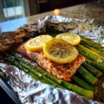 Close-up of a delicious baked salmon & asparagus foil packet, topped with lemon slices and herbs.