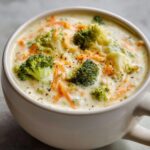 Close-up of a bowl of creamy Broccoli Cheddar Soup with broccoli florets and shredded carrots.