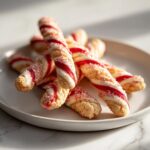 A pile of twisted candy cane cookies, decorated with red and white stripes and sprinkled with red sugar.