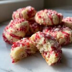 Close-up of a pile of festive Candy Cane Shortbread Cookies, one broken in half to show the crumbly texture and red and white swirls.