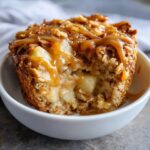 Close-up of a Caramel Apple Cinnamon Oatmeal Bake in a white bowl, drizzled with caramel.