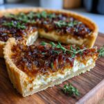 Close-up of a slice of Caramelized Onion Tart with golden crust and topping, garnished with fresh herbs.