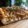 Close-up of a slice of Caramelized Onion Tart, showing flaky crust and caramelized onions.