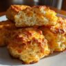 Close-up of golden Cheddar Biscuits on a white plate, showing a flaky texture.