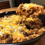 Close-up of a One-Pot Cheesy Beef and Rice Skillet with melted cheese, showing a cheese pull.