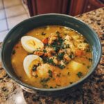 Close-up of a bowl of Chicken & Rice Comfort Soup with egg halves and herbs.