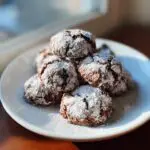 Pile of Chocolate Peppermint Snowball Cookies dusted with powdered sugar on a white plate.