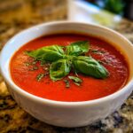 Close-up of a bowl of Classic Tomato Basil Soup garnished with fresh basil leaves.
