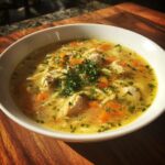 A bowl of Cozy Lemon Chicken Orzo Soup with chicken, orzo pasta, carrots, and herbs.