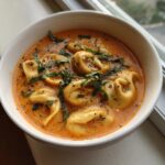 Close-up of a bowl of Creamy Tomato Tortellini Soup garnished with fresh basil.