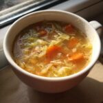 A close-up of a bowl of Detox Cabbage & Carrot Soup, with visible carrots and cabbage.