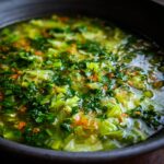 Close-up of a bowl of Detox Green Vegetable Soup, showing fresh green vegetables and herbs.