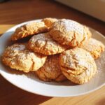 A pile of golden Easy 3-Ingredient Christmas Cookies dusted with powdered sugar on a white plate.