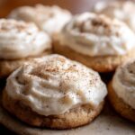 Close-up of frosted eggnog sugar cookies with white frosting and a sprinkle of cinnamon.