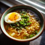 Close-up of a bowl of Garlic Miso Ramen-Inspired Broth with noodles, egg, and green onions.