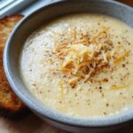Close-up of a bowl of Garlic Parmesan Cauliflower Soup with grated cheese and toasted bread.