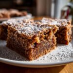 Close-up of moist Gingerbread Cookie Bars dusted with powdered sugar on a white plate.