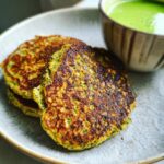 Close-up of a stack of Green Smoothie Oatmeal Pancakes on a plate with a side of green smoothie.