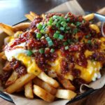 Close-up of a plate of Hearty Chili Cheese Fries topped with chili, cheese, and green onions.