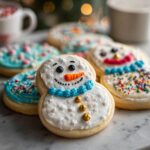 Close-up of adorable Melted Snowman Sugar Cookies decorated with white icing, orange carrot noses, and colorful sprinkles.