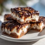 Close-up of stacked North Pole Chocolate-Dipped Shortbread Bars on a white plate, drizzled with chocolate.