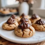 Close-up of Santa's Favorite Peanut Butter Blossoms cookies with chocolate kisses on a white plate.