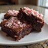 Close-up of three Peppermint Hot Cocoa Brownies on a white plate, topped with crushed peppermint candies.