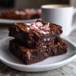 Two delicious Peppermint Hot Cocoa Brownies stacked on a white plate, topped with crushed peppermint.
