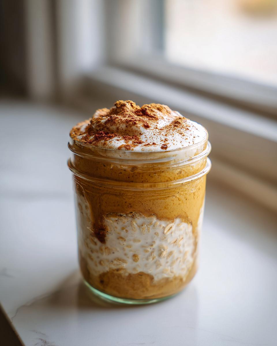 Close-up of Pumpkin Spice Latte Overnight Oats in a jar, topped with whipped cream and cinnamon.