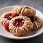Close-up of delicious Raspberry Thumbprint Cookies with Icing, drizzled with white icing and filled with raspberry jam.