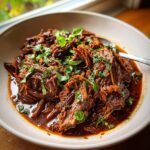 Close-up of a bowl of Rustic Red Wine Pot Roast, garnished with fresh herbs.