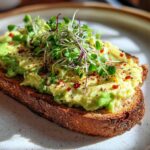 A slice of toasted bread topped with creamy avocado, chia seeds, chili flakes, and fresh microgreens, representing Savory Chia Pudding Avocado Toast.