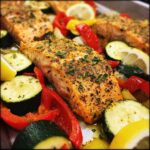 Close-up of a sheet pan with Sheet Pan Turmeric Salmon, zucchini, bell peppers, and lemon wedges.