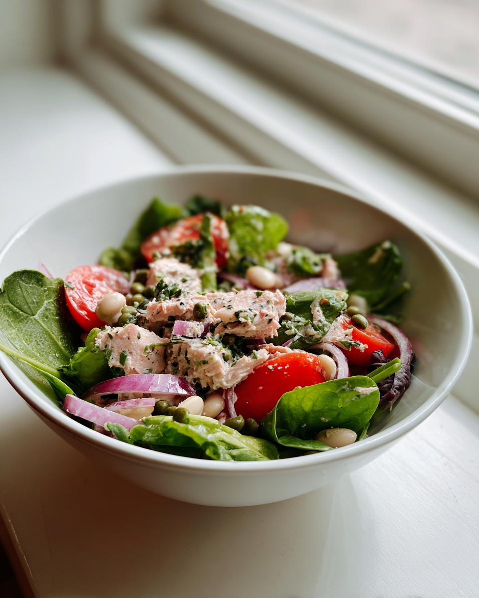 Close-up of a Simple Tuna and White Bean Salad in a white bowl with tomatoes and red onion.