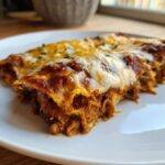 A close-up of a slice of Slow Cooker Bean and Cheese Enchiladas on a white plate, with melted cheese.