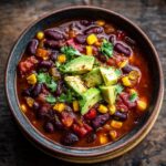 Close-up of a bowl of Spicy Black Bean & Corn Soup, garnished with avocado and cilantro.