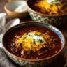 Two bowls of Spicy Black Bean & Corn Soup topped with cheese and sour cream.