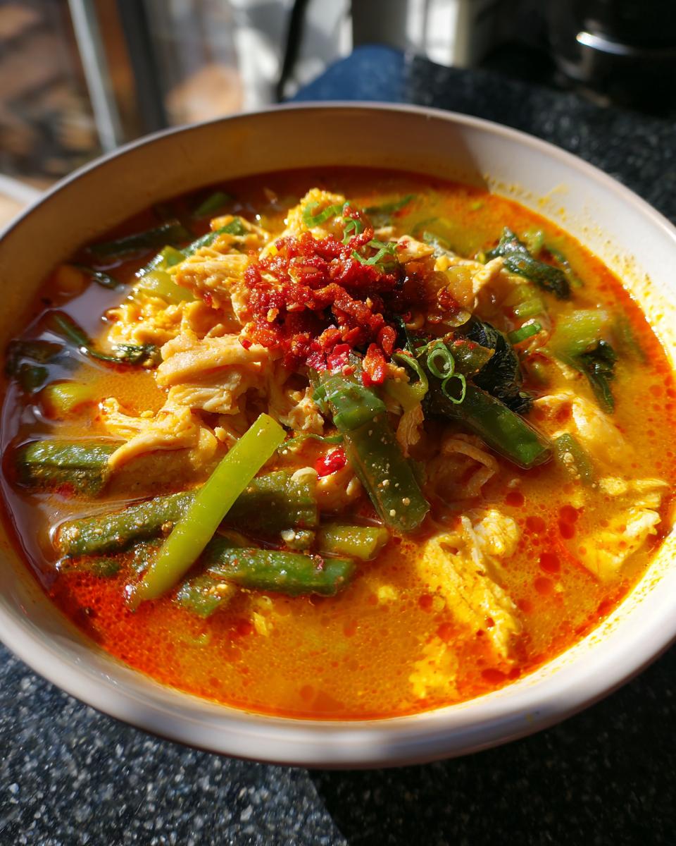 Close-up of a bowl of Spicy Thai Chicken Soup with chicken, vegetables, and chili topping.